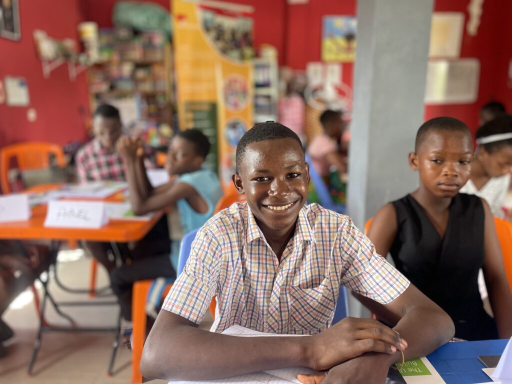 A smiling boy at his desk in a busy, colourful classroom.